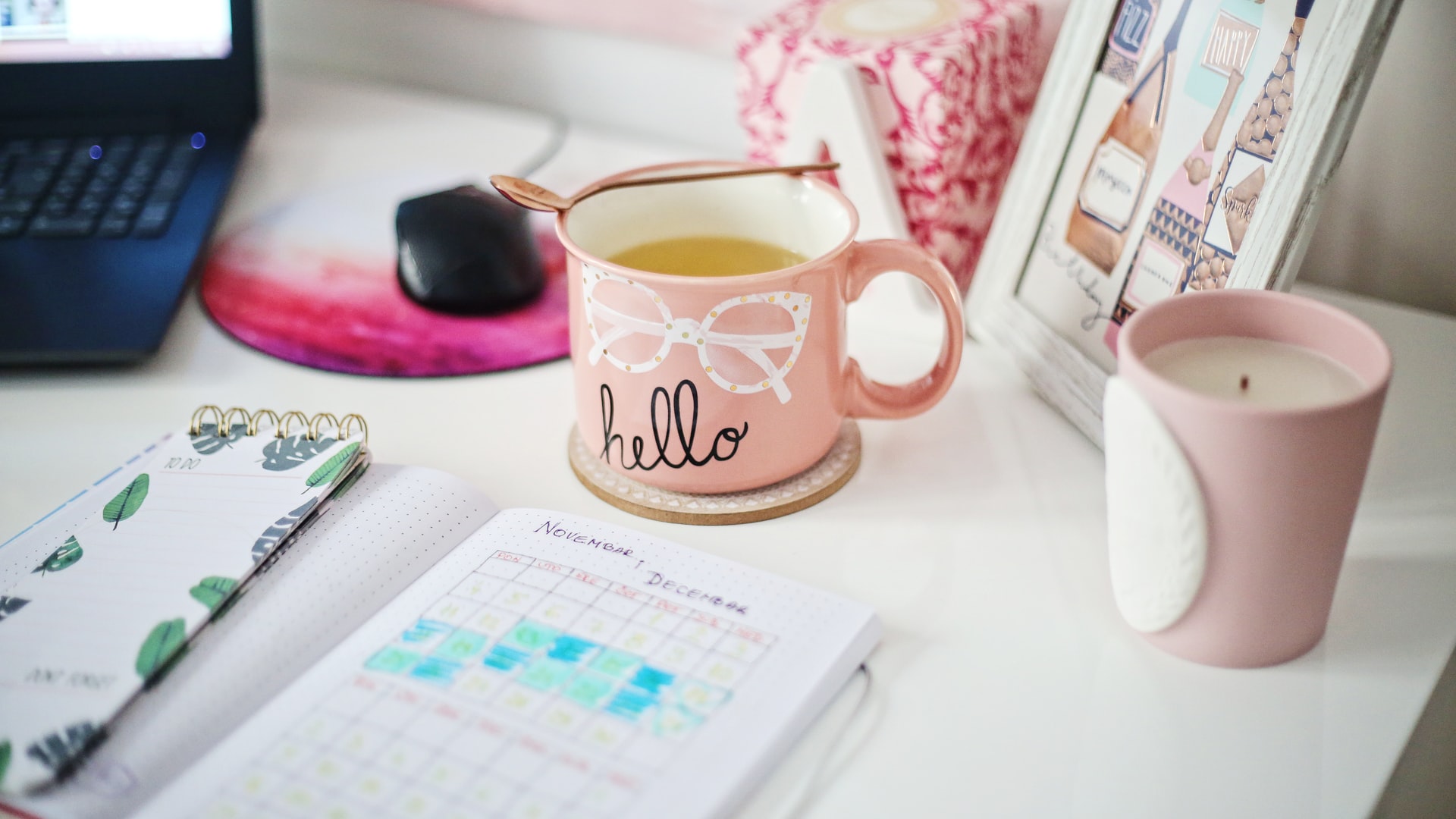 Desk with a laptop computer, mouse, hot drink, a candle and a calendar