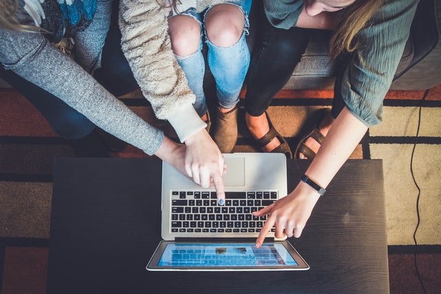 group of people leaning over to a laptop on a table group of people leaning over to a laptop on a table