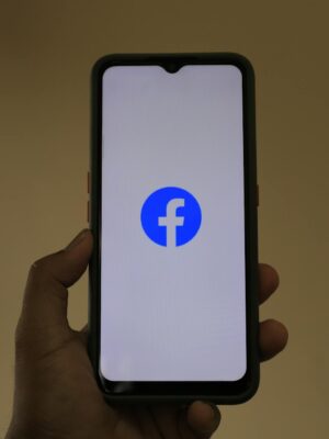 A smartphone held in hand showing the Facebook logo on its screen.